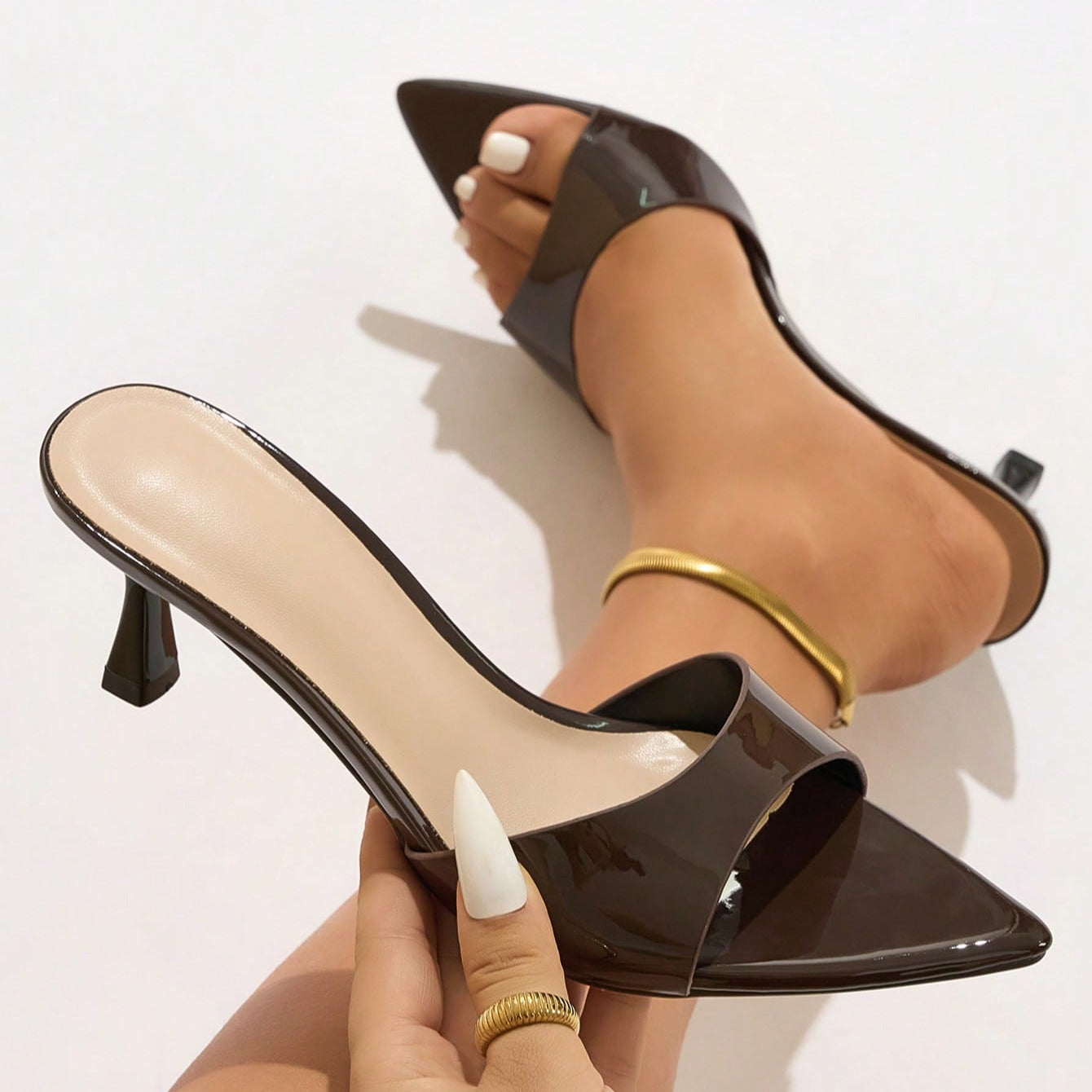 Mescini - Brown glossy pointed toe mule held in hand next to the foot, close view, US sizes