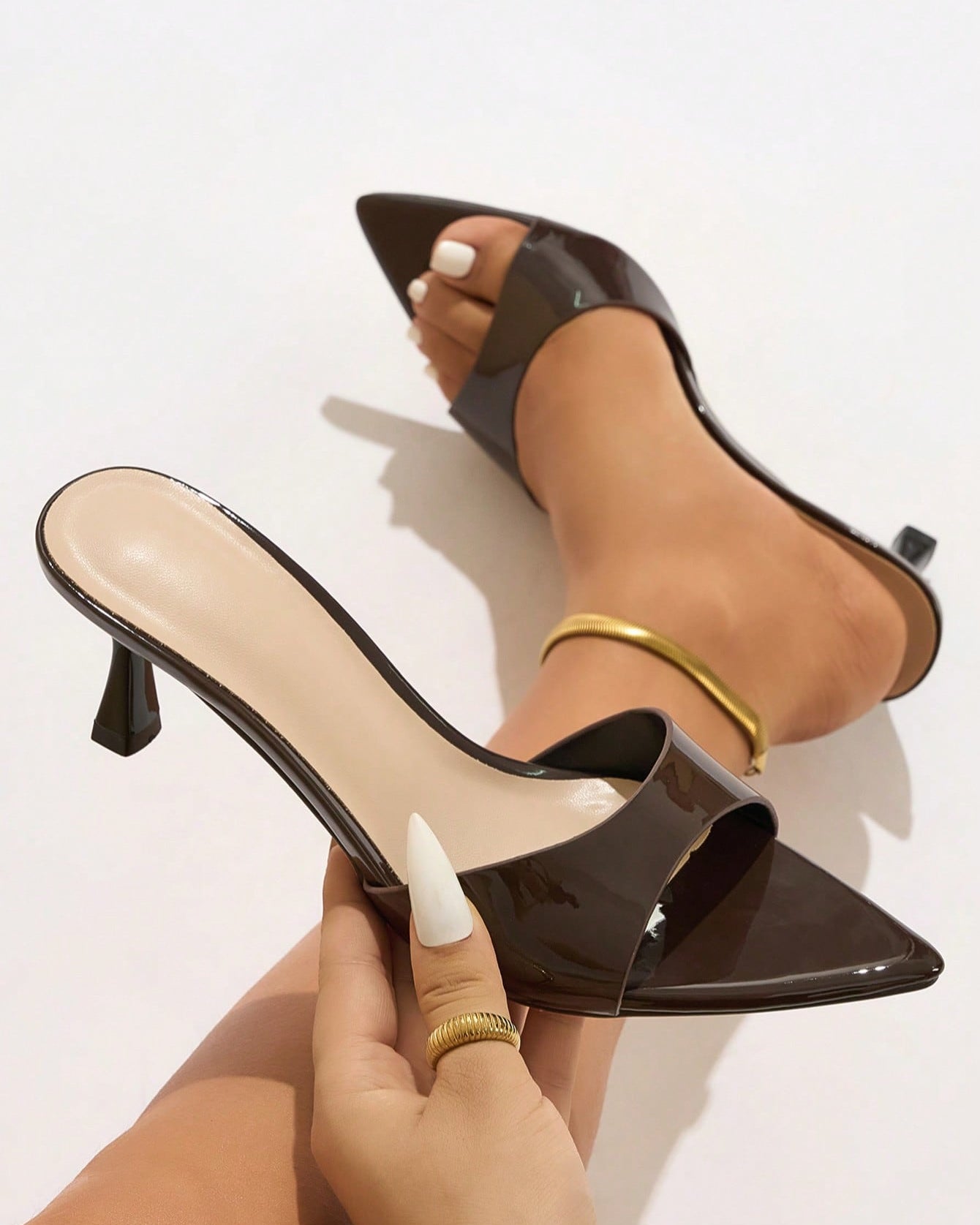 Mescini - Brown glossy pointed toe mule held in hand next to the foot, close view, US sizes