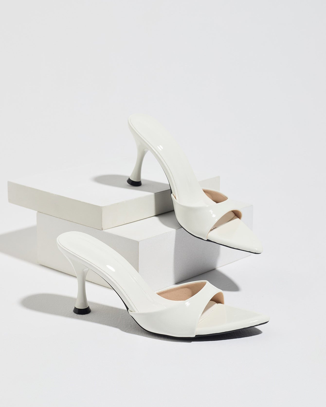 Mescini - White pointed toe mule heels as a pair on white risers, studio view, US sizes