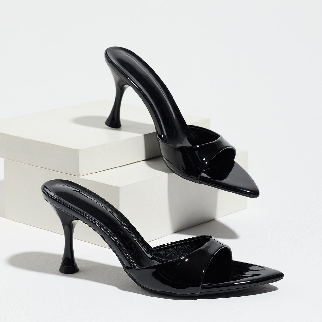 Mescini - Black pointed toe mule heels as a pair on white risers, studio view, US sizes