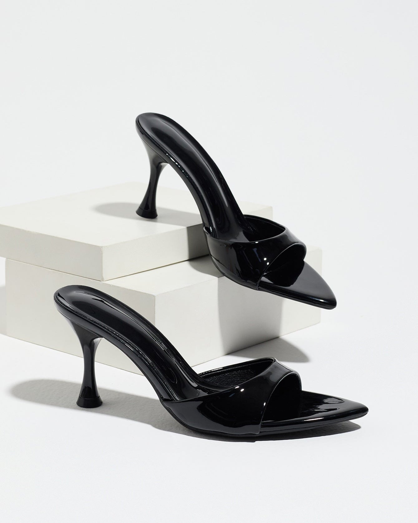 Mescini - Black pointed toe mule heels as a pair on white risers, studio view, US sizes