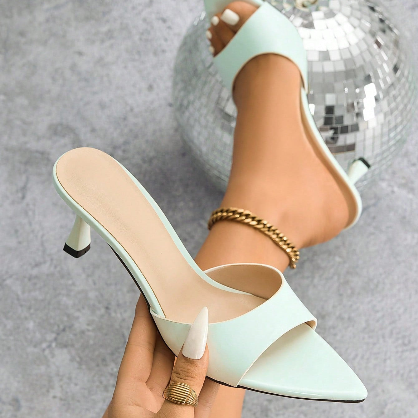 Mescini - White pointed toe kitten heel mule held in hand beside the foot, close up, US