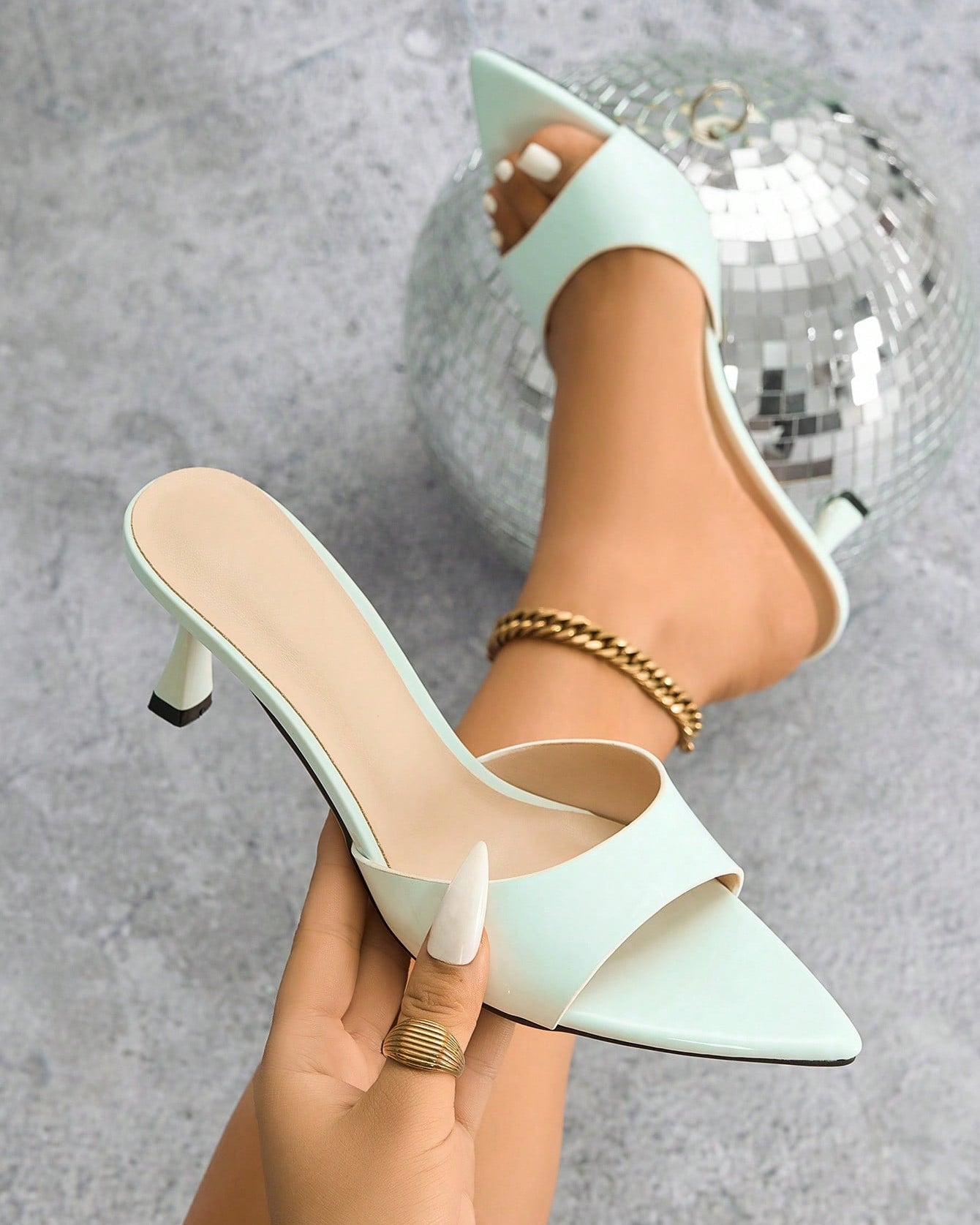 Mescini - White pointed toe kitten heel mule held in hand beside the foot, close up, US