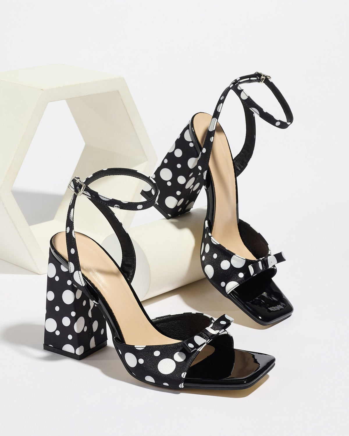 Mescini - Black polka dot block heel sandal pair beside a white riser, studio view, US