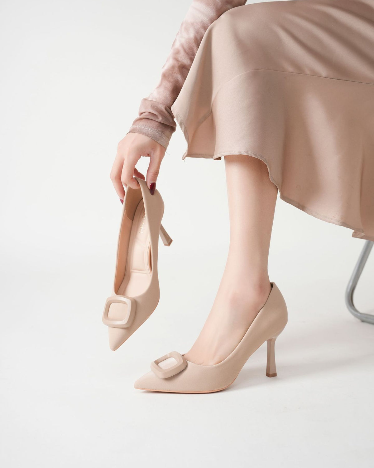 Mescini beige square ring pointed toe pumps, model holding one by the strap, US women's sizes