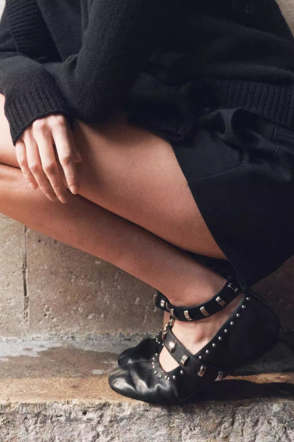 Mescini black studded ankle strap mary jane flats worn by a model on a stone step, US women's sizes