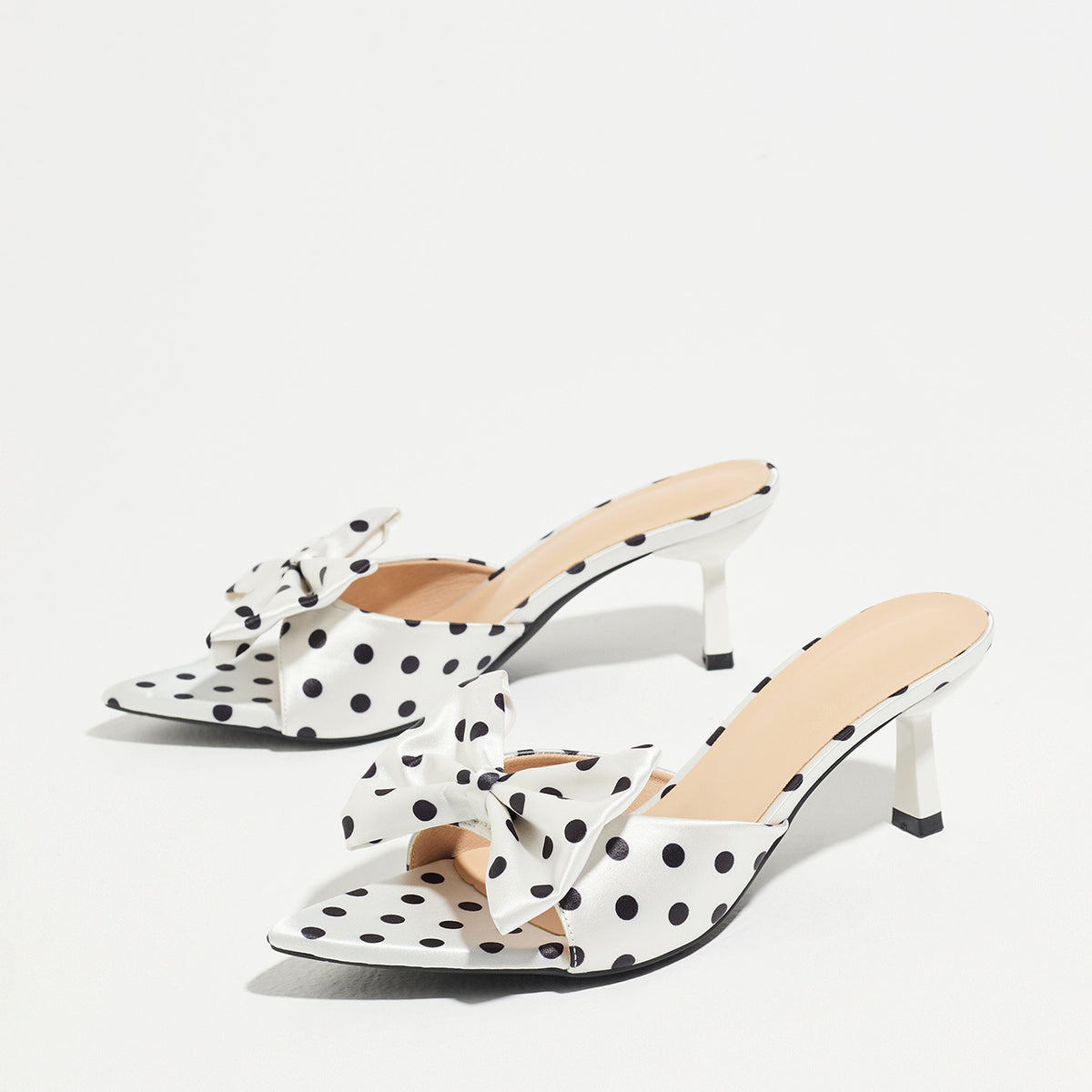 Mescini white polka dot bow pointed mule heels, pair angled on a pale grey background, US women's sizes