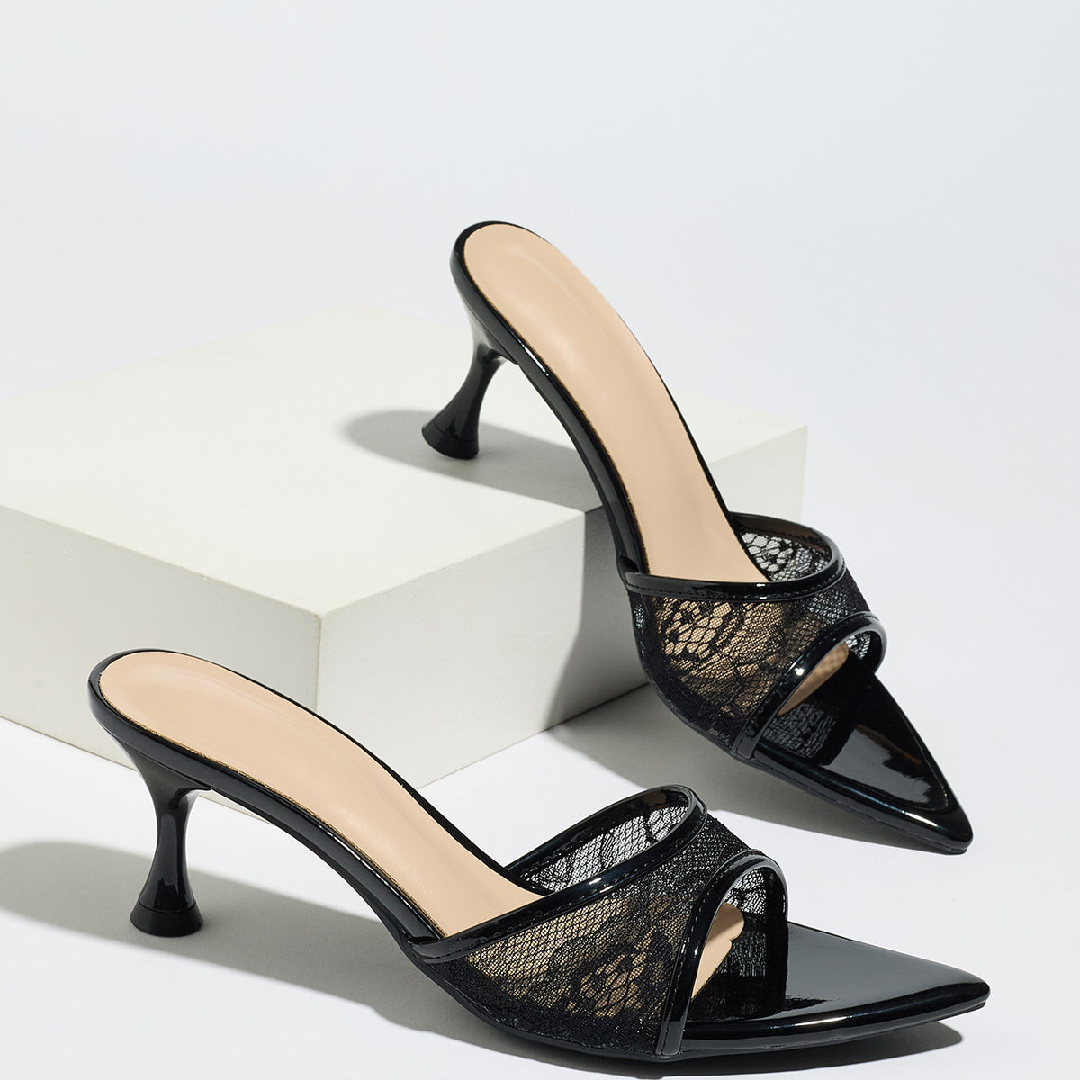 Mescini black sheer lace pointed toe mule heels, pair staged on white display blocks, US women's sizes