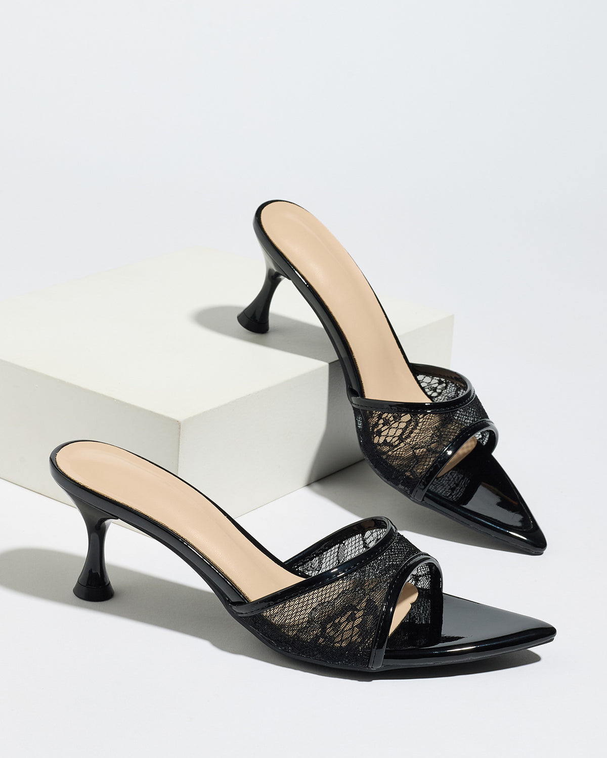 Mescini black sheer lace pointed toe mule heels, pair staged on white display blocks, US women's sizes