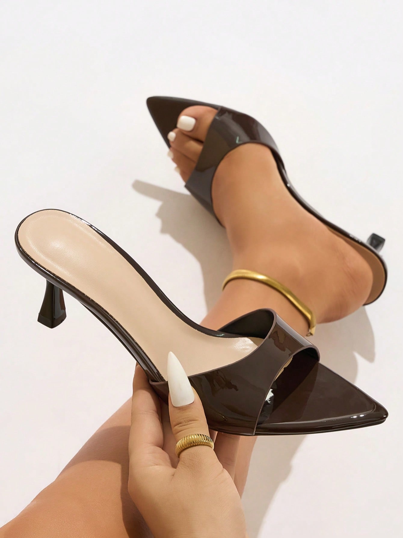 Mescini - Brown glossy pointed toe mule held in hand next to the foot, close view, US sizes