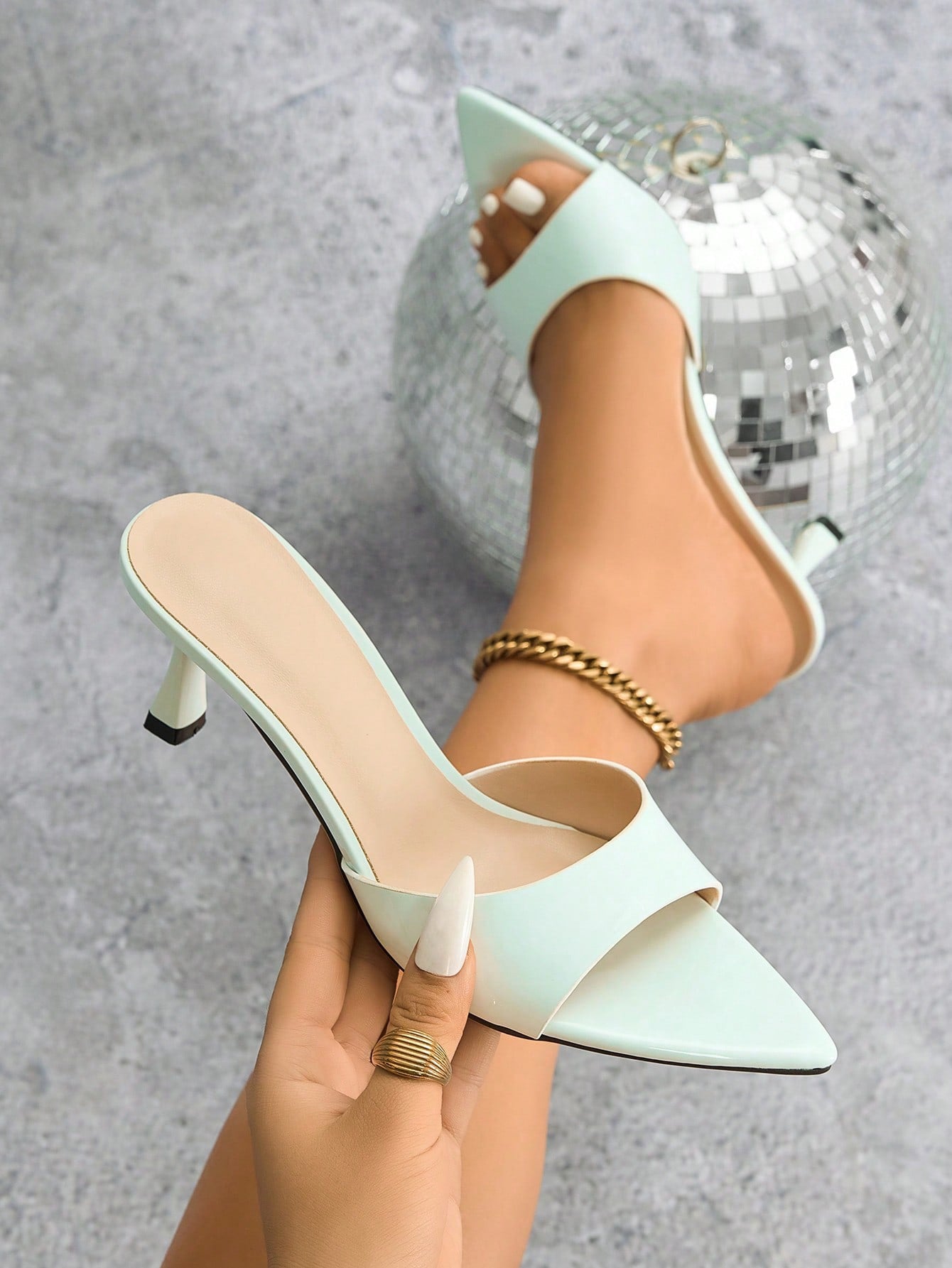 Mescini - White pointed toe kitten heel mule held in hand beside the foot, close up, US