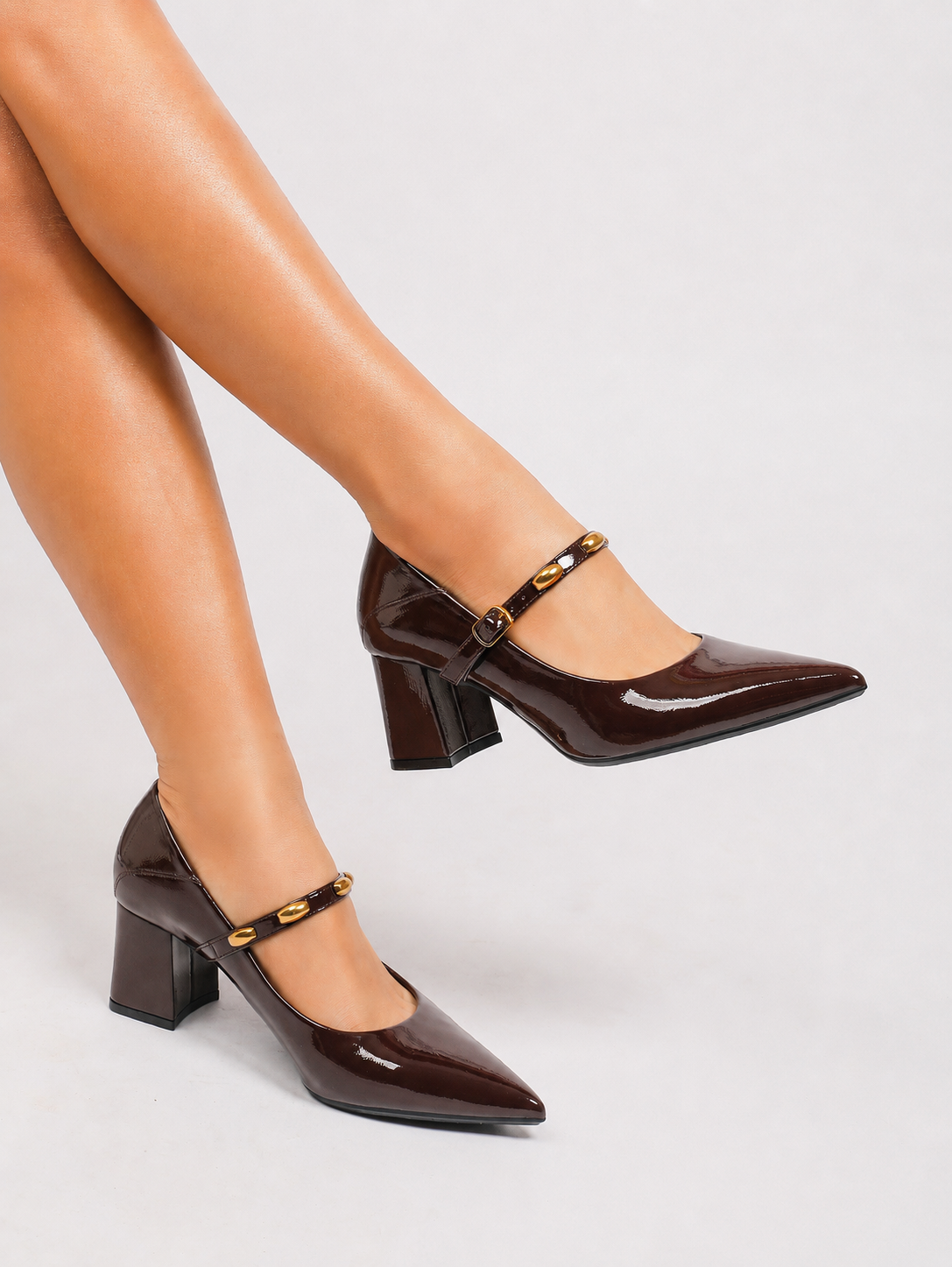 Mescini brown studded strap Mary Jane heels, worn with legs crossed and one foot raised, US women's sizes