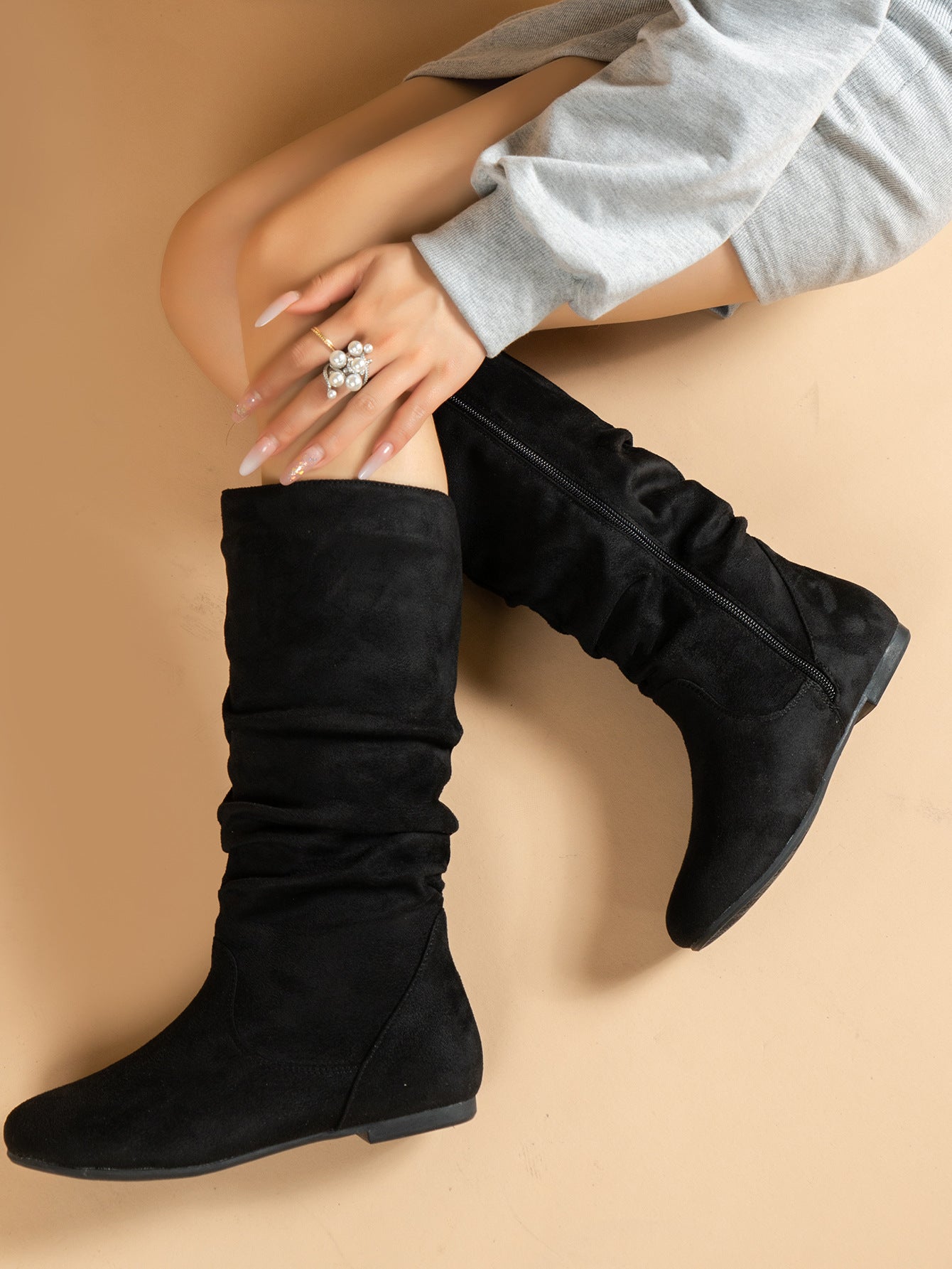 Mescini black pleated slouch flat mid calf boots, worn by a model seated on the floor, US women's sizes