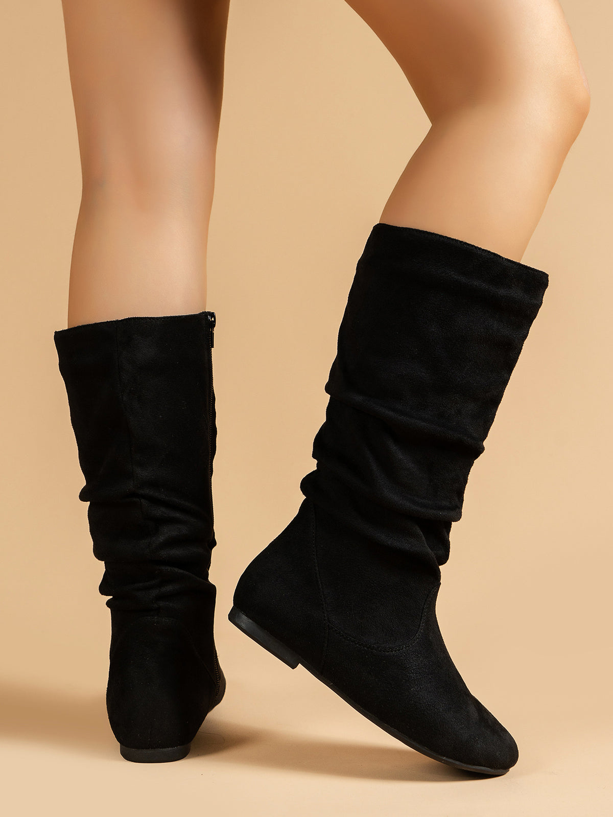 Mescini black pleated slouch flat mid calf boots, worn from behind on a tan backdrop, US women's sizes