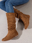 Mescini brown pleated slouch flat mid calf boots, worn with jeans by a seated model, US women's sizes