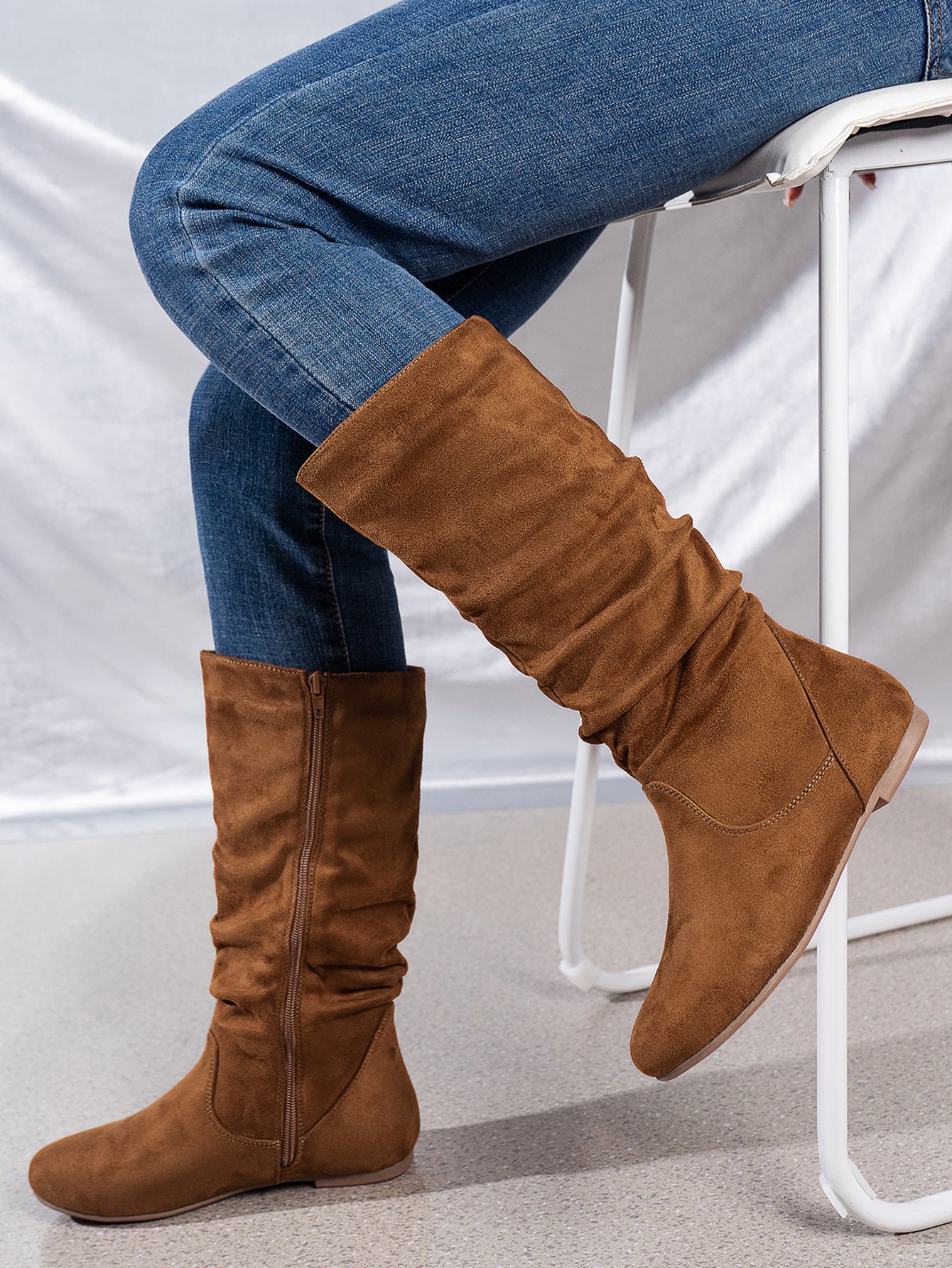 Mescini brown pleated slouch flat mid calf boots, worn with jeans beside a chair, US women's sizes