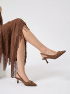 Mescini brown buckle strap pointed slingback heels, worn seated with a fringed skirt, US women's sizes