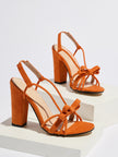 Mescini orange knotted bow strappy block heel sandals, pair posed on a white riser, US women's sizes