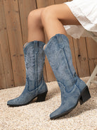 Mescini dark blue embroidered western cowboy boots, worn by a seated model on gravel, US women's sizes