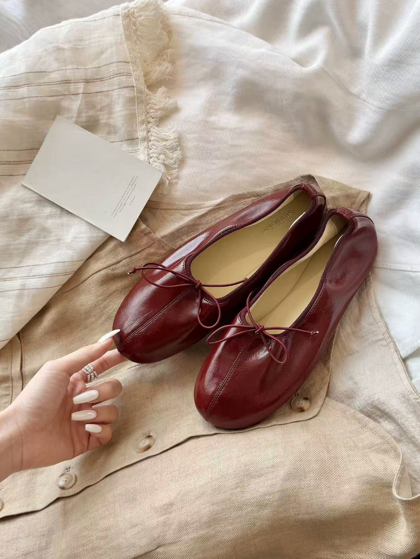 Mescini burgundy soft drawstring bow ballet flats, pair on linen with a hand reaching in, US women's sizes