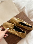 Mescini yellow soft drawstring bow ballet flats, pair on a wooden board beside a hand, US women's sizes