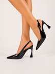 Mescini black pointed toe patent slingback pumps worn with legs crossed, US women's sizes