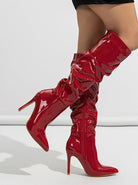 Mescini red ruched patent knee high stiletto boots, worn kneeling on a white set, US women's sizes