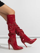 Mescini red ruched patent knee high stiletto boots, worn by a seated model, legs bent, US women's sizes