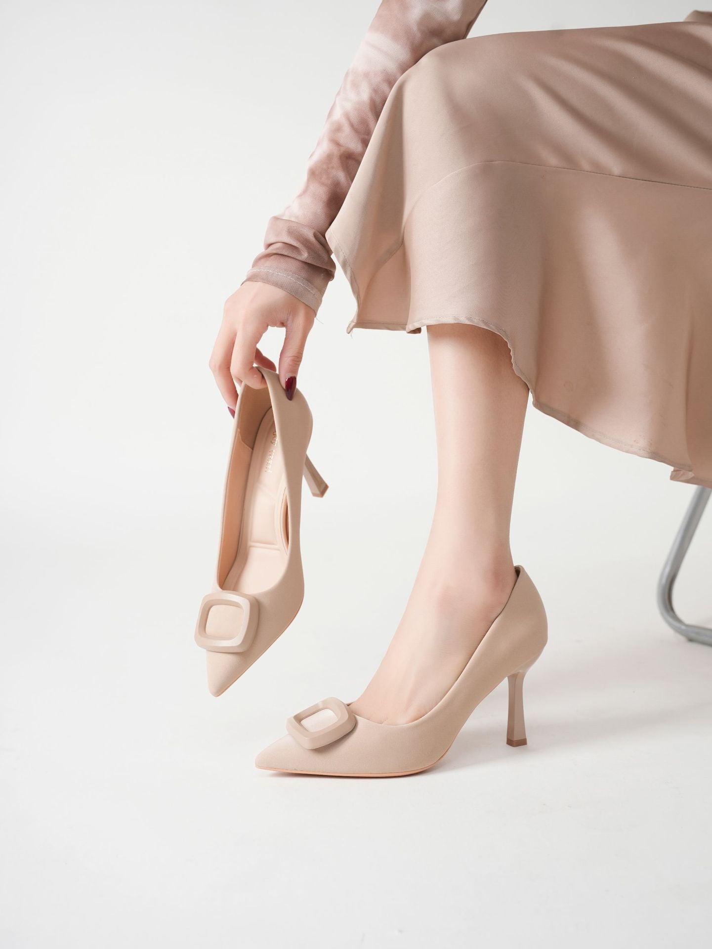 Mescini beige square ring pointed toe pumps, model holding one by the strap, US women's sizes