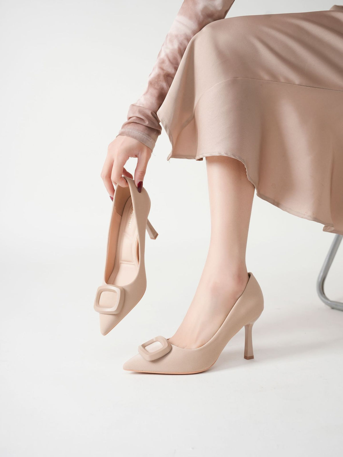 Mescini beige square ring pointed toe pumps, model holding one by the strap, US women's sizes