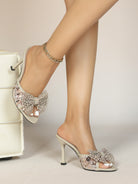Mescini apricot crystal bow square toe mules, worn by a seated model on a pale block, US women's sizes