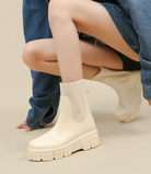 Mescini ivory glossy platform chelsea rain boots, worn crouching in wide leg jeans, US women's sizes