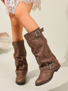 Mescini brown ruched buckle knee high riding boots, worn standing against a pale wall, US women's sizes