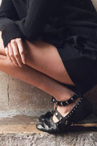 Mescini black studded ankle strap mary jane flats worn by a model on a stone step, US women's sizes