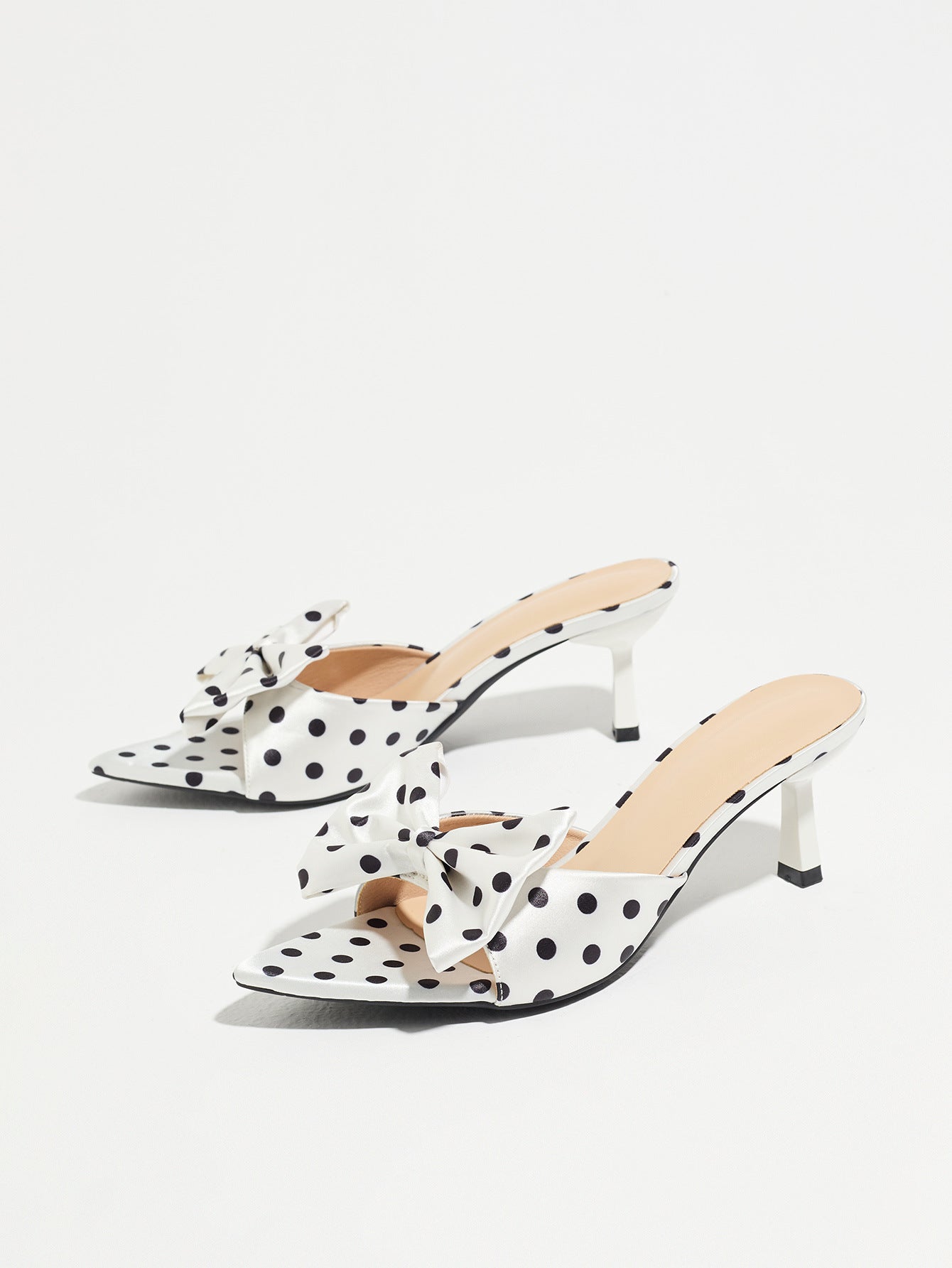 Mescini white polka dot bow pointed mule heels, pair angled on a pale grey background, US women's sizes