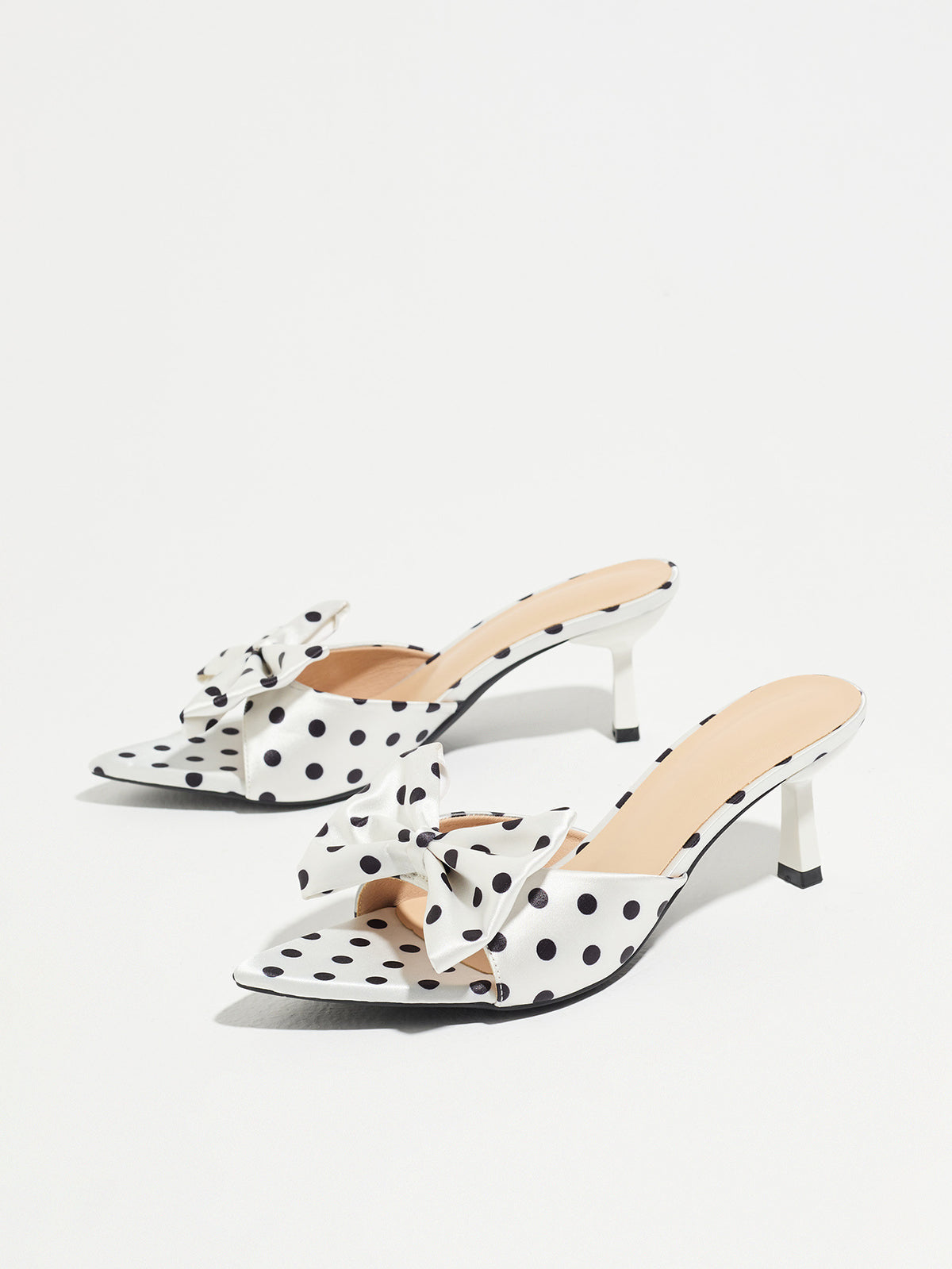 Mescini white polka dot bow pointed mule heels, pair angled on a pale grey background, US women's sizes