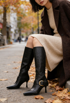 Mescini black buckled pointed toe knee high boots, worn seated on an autumn street, US women's sizes