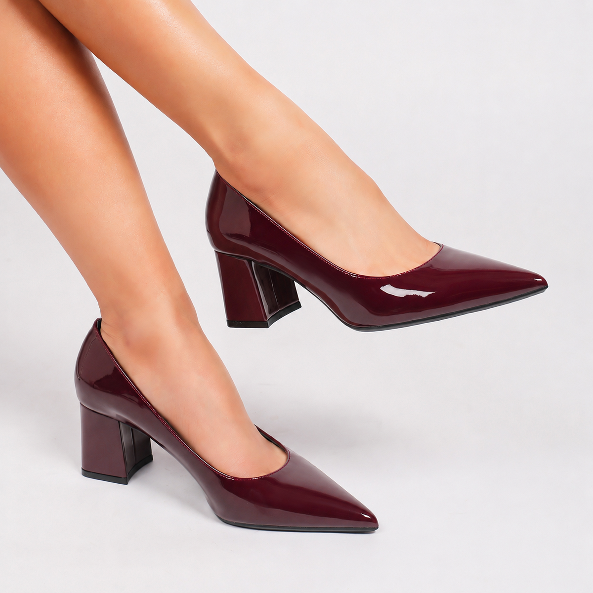 Mescini burgundy high shine pointed toe block heel pumps, worn on a model with legs crossed, US women's sizes