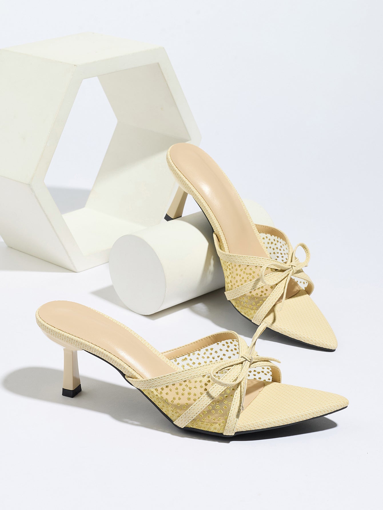 Mescini apricot bow mesh pointed toe mule heels, the pair beside white display blocks, US women's sizes