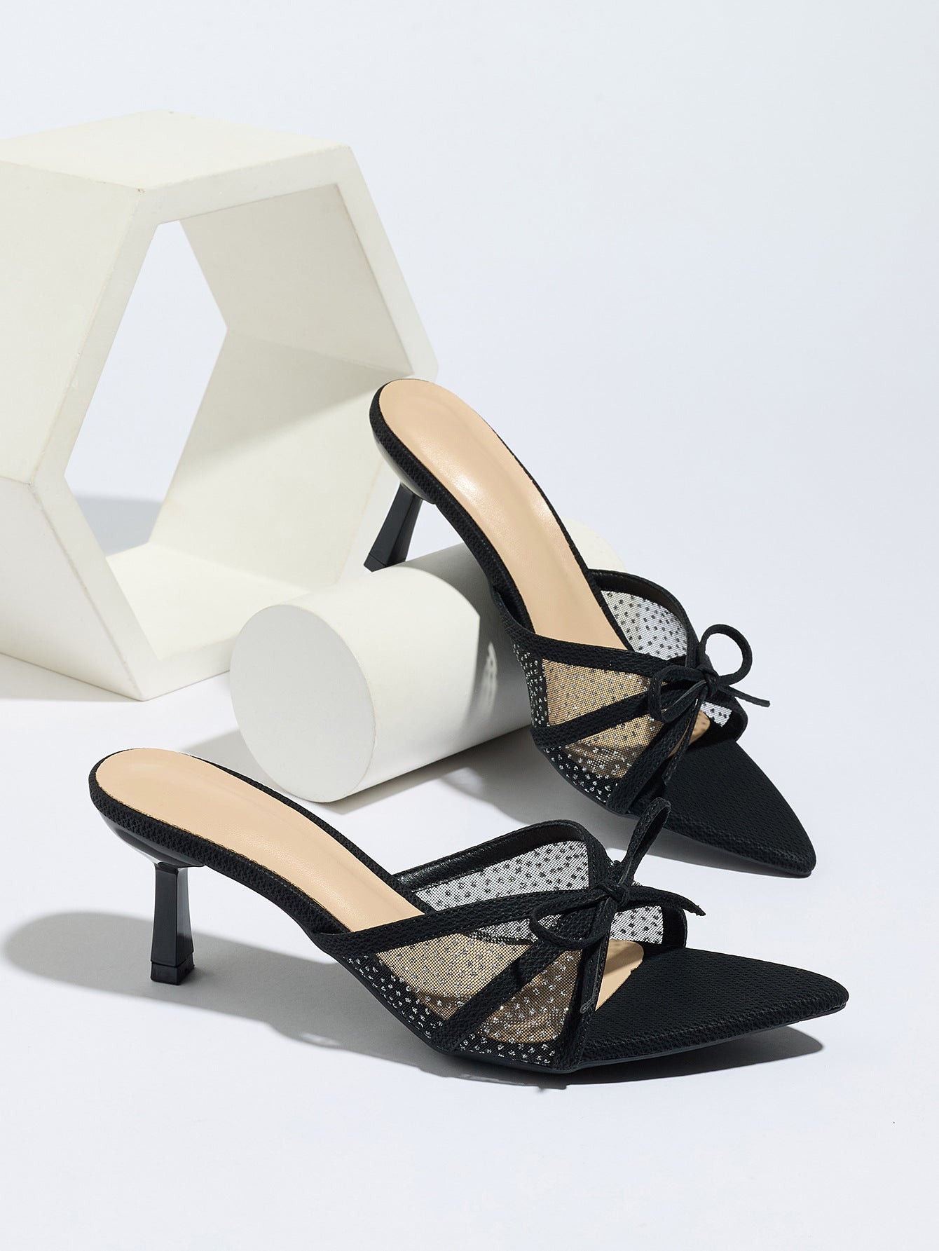 Mescini black bow mesh pointed toe mule heels, the pair beside white display blocks, US women's sizes