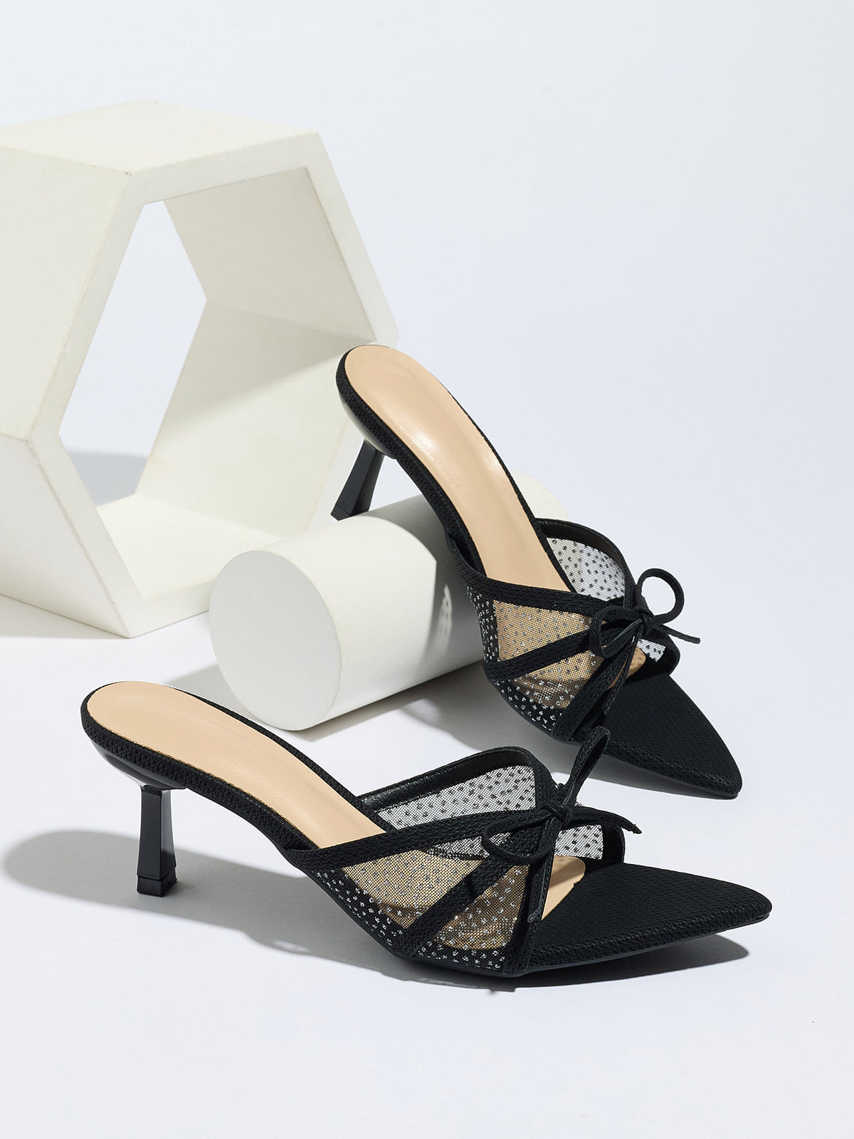 Mescini black bow mesh pointed toe mule heels, the pair beside white display blocks, US women's sizes