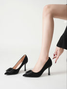 Mescini black pointed toe stiletto pumps, worn on a model reaching for the buckle, US women's sizes