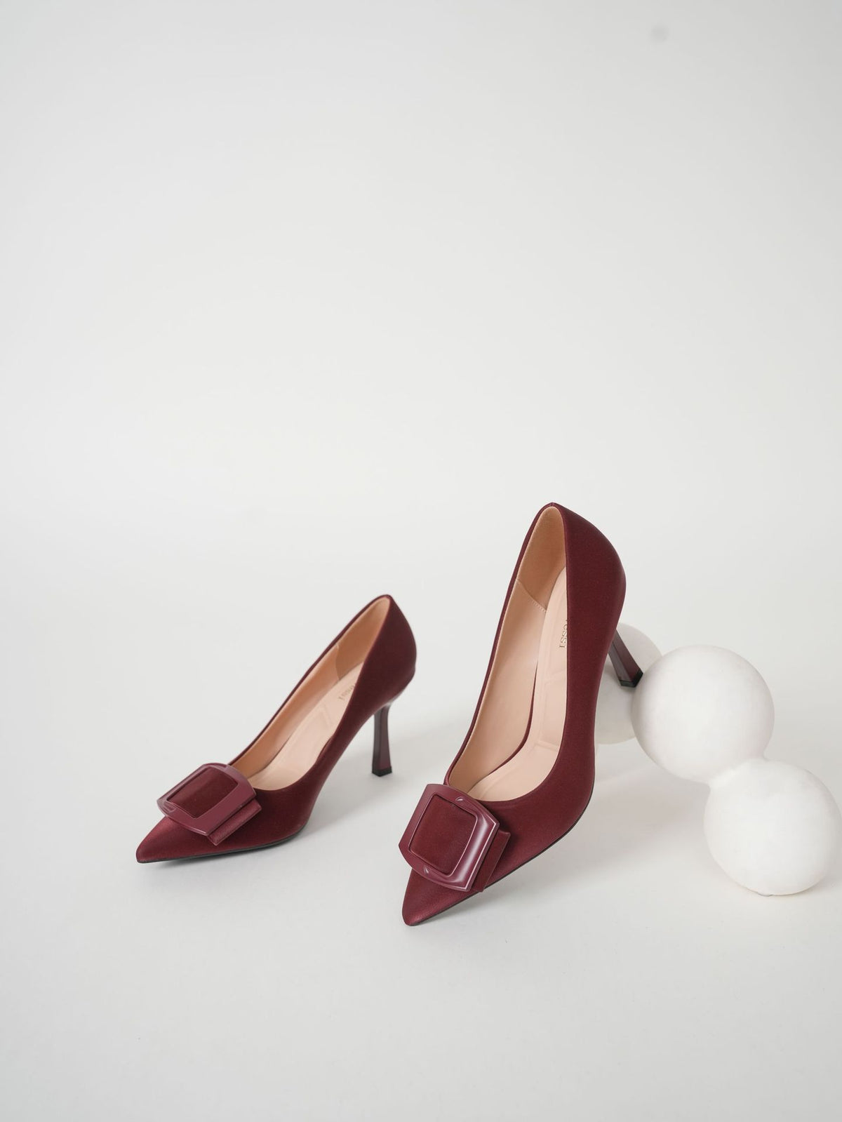 Mescini burgundy pointed toe stiletto pumps, pair posed with two white spheres, US women's sizes
