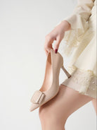 Mescini beige pointed toe stiletto pumps, model easing her foot into the shoe, US women's sizes