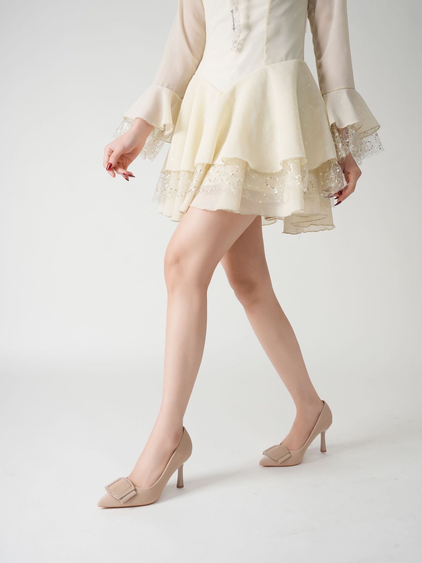 Mescini beige pointed toe stiletto pumps, worn by a model walking in a cream dress, US women's sizes