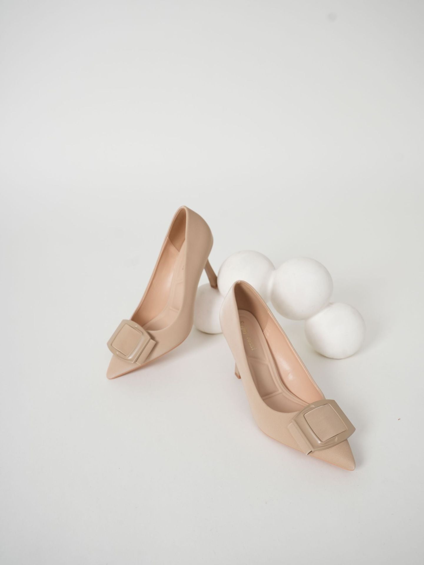 Mescini beige pointed toe stiletto pumps, pair standing next to white wool spheres, US women's sizes