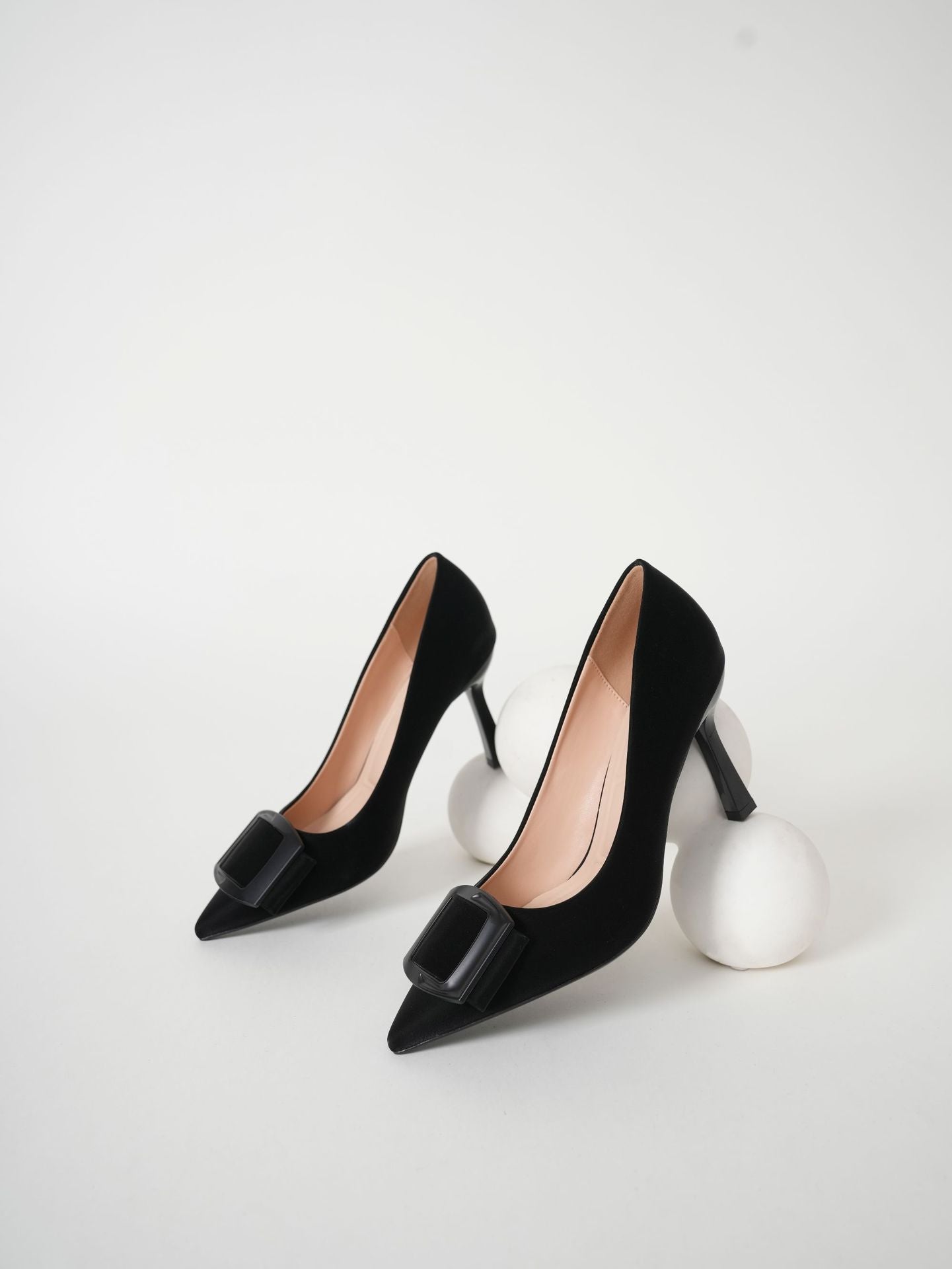 Mescini black pointed toe stiletto pumps, pair styled beside white wool spheres, US women's sizes