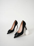 Mescini black pointed toe stiletto pumps, pair styled beside white wool spheres, US women's sizes