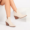 Mescini beige V-cut pointed toe block heel ankle boots, worn by a seated model, US women's sizes