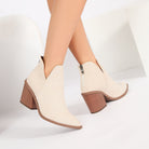 Mescini beige V-cut pointed toe ankle boots worn with legs crossed, side view, US women's sizes
